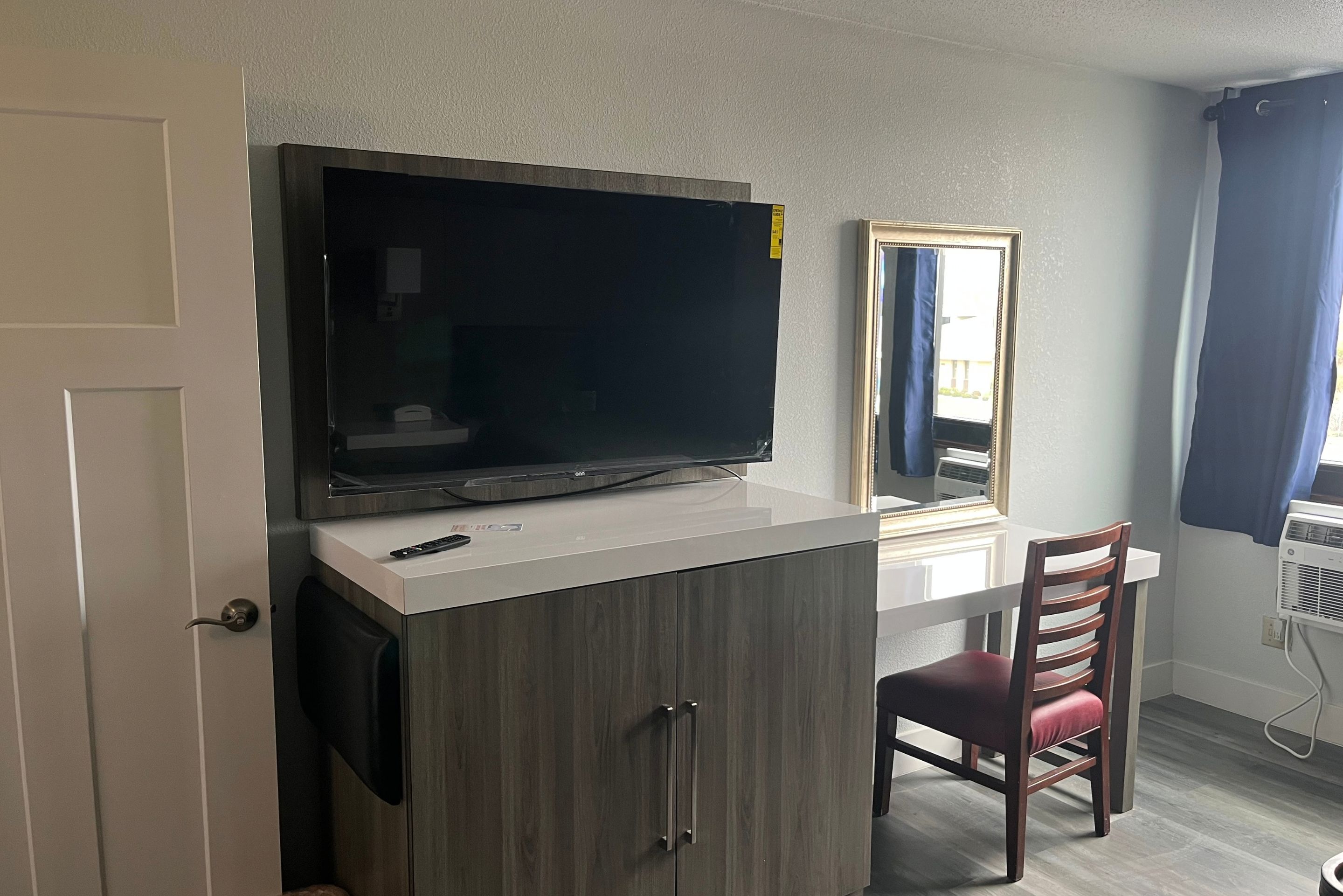 A room with a television on a white cabinet, a mirror, a chair, and a door.