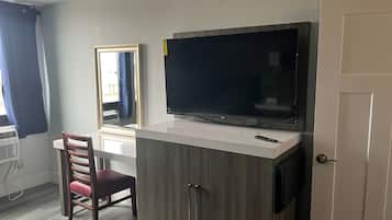 Una habitación con televisión montada en un mueble, una silla y un ventanal con cortinas.