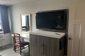 A room with a TV mounted on a cabinet, a chair, and a window with curtains. - Coratel Inn and Suites By Jasper Roseville (Roseville)