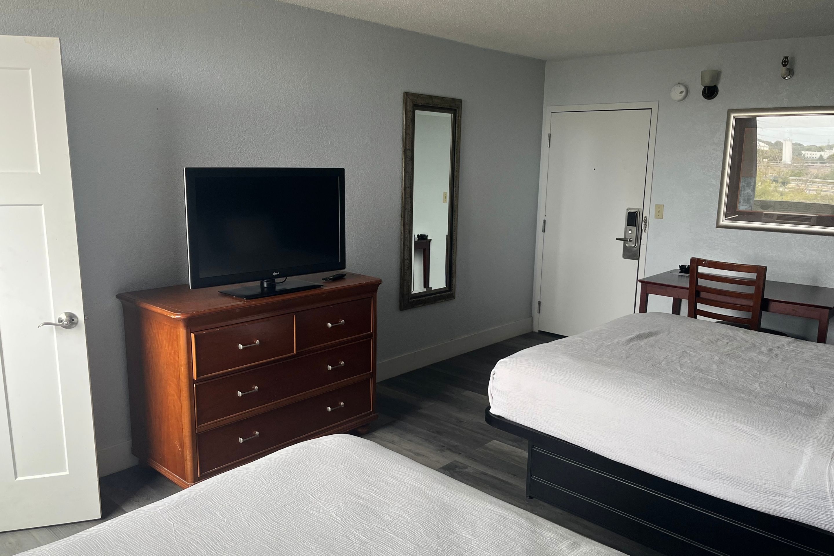 Quarto de hotel com cama, televisão em uma cômoda, escrivaninha e uma cadeira.