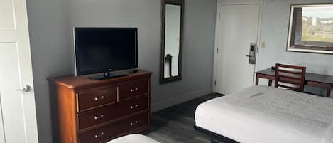A hotel room with a bed, a TV on a dresser, a desk, and a chair.