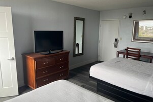 Una habitación de hotel con una cama, un televisor en una cómoda, un escritorio y una silla.
