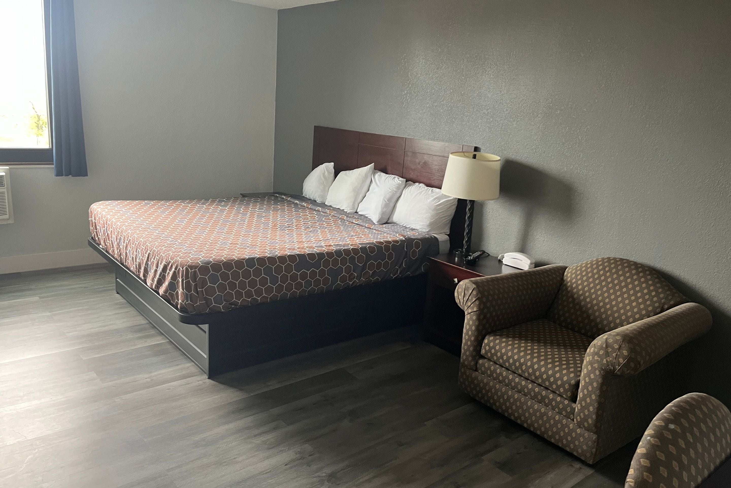Une chambre d’hôtel avec un lit, une chaise, une table de chevet et une lampe.
