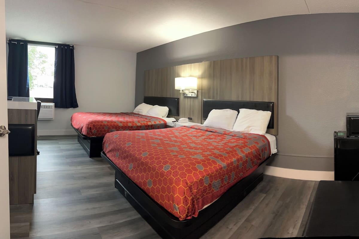 A hotel room with two beds, a desk, a chair, and a lamp.