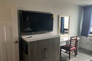 A room with a television on a white cabinet, a mirror, a chair, and a door. - Coratel Inn and Suites By Jasper Roseville (Roseville)