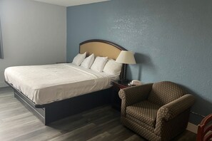 A hotel room with a bed, a chair, a nightstand, and a lamp. - Coratel Inn and Suites By Jasper Roseville (Roseville)