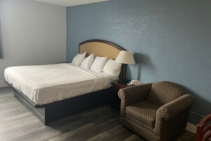Una habitación de hotel con una cama, una silla, una mesita de noche y una lámpara.