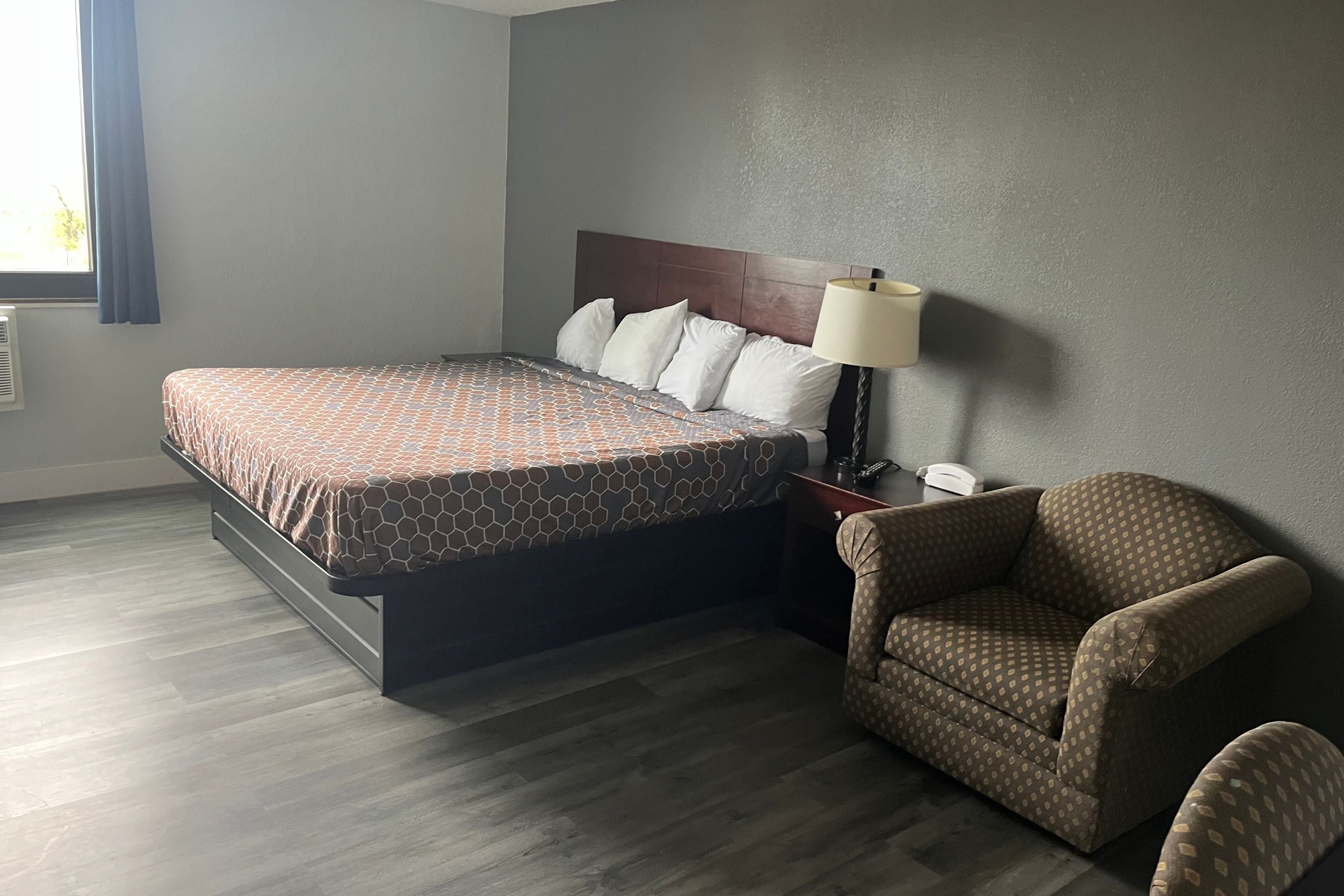 Una habitación de hotel con una cama, una silla, una mesita de noche y una lámpara.