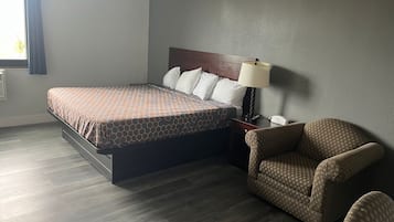 Una habitación de hotel con una cama, una silla, una mesita de noche y una lámpara.