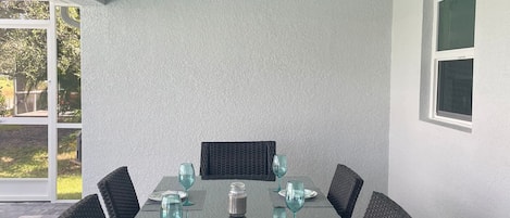 Un coin repas avec une table dressée pour six personnes, entouré de chaises en osier, d’un ventilateur de plafond et offrant une vue sur l’extérieur.