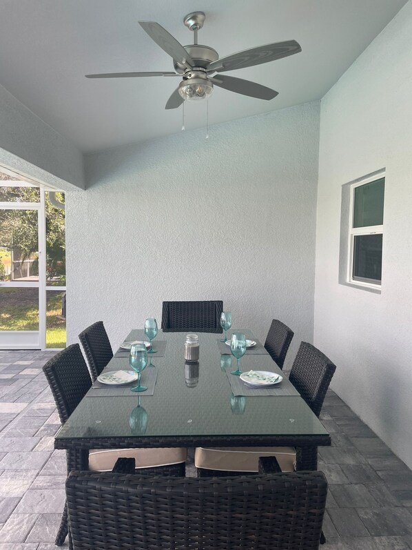 A dining area with a table set for six, surrounded by wicker chairs, a ceiling fan, and a view of the outdoors. - 2 BR Canal-Front Paradise, Heated Pool, Beaches & Gulf Coast (Rotonda West)