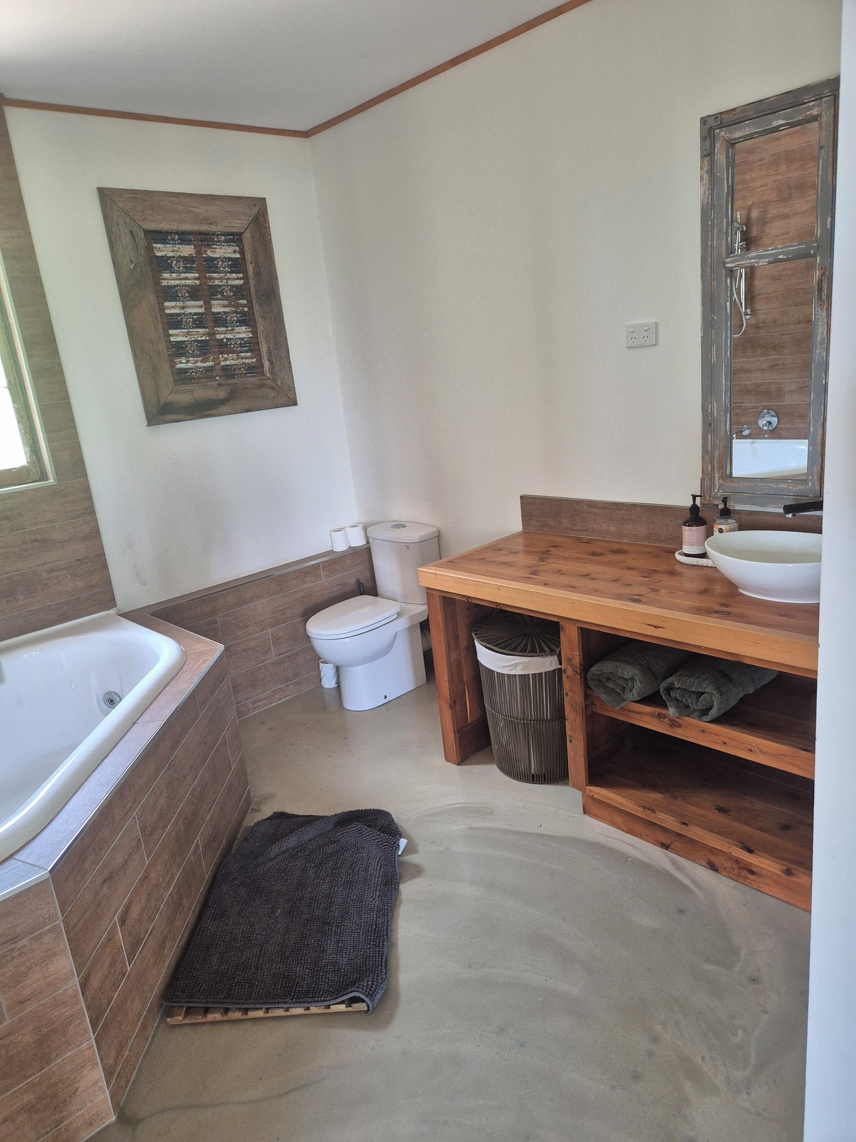 Een badkamer met een houten wastafelmeubel, een wit toilet, een bad en een grote spiegel.