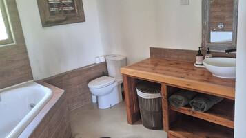 Een badkamer met een houten wastafelmeubel, een wit toilet, een bad en een grote spiegel.
