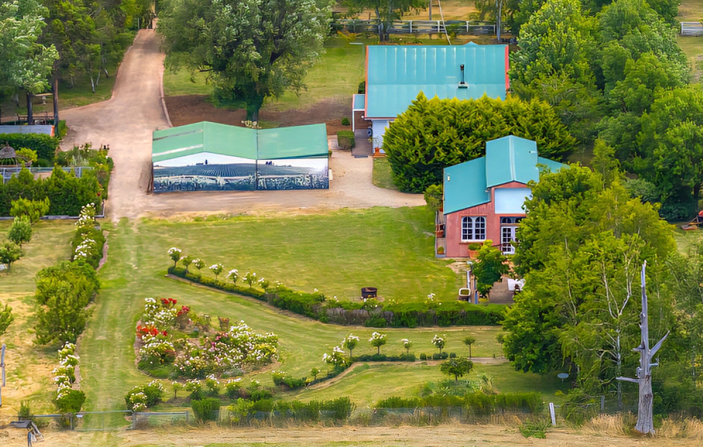 Luchtbeeld van een landgoed met een onverharde weg, groene velden en een groot gebouw met een blauw dak.