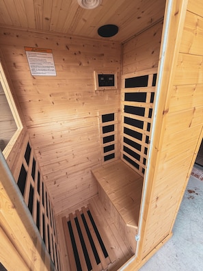 Sauna, jossa on puuseinät ja -lauteet, ohjauspaneeli ja varoitusmerkki.