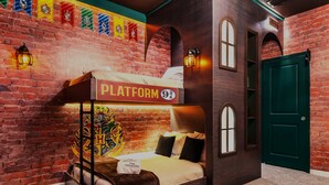 Una habitación de hotel temática con pared de ladrillo, una cama litera con la etiqueta 'PLATFORM 9¾' y el escudo de Hogwarts.