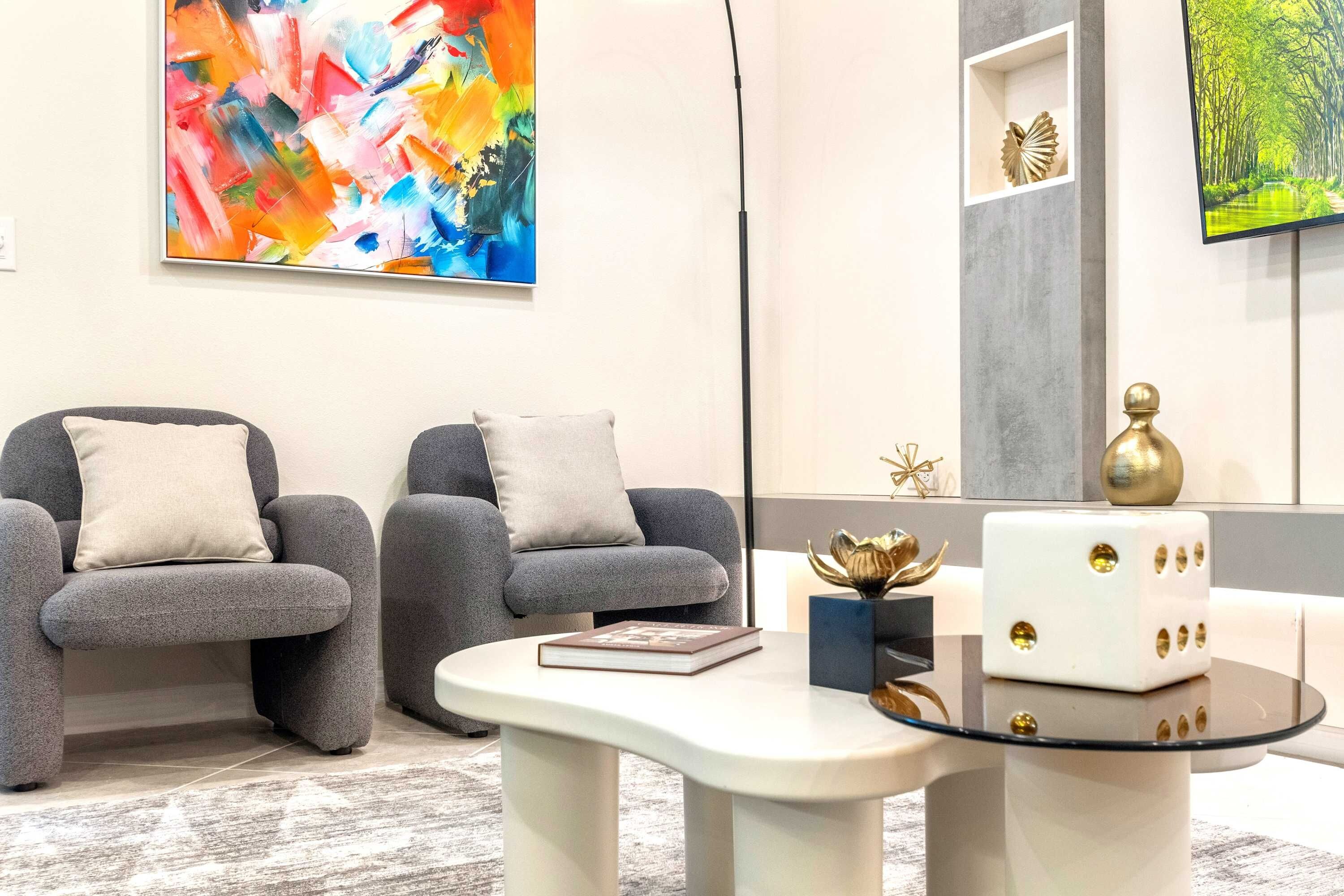 A modern living room with two grey armchairs, a white coffee table, and a large abstract painting on the wall.