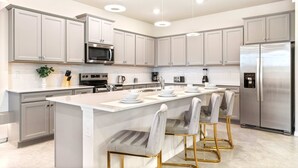 Una cocina moderna con armarios grises, electrodomésticos de acero inoxidable y una isla central con taburetes de bar.