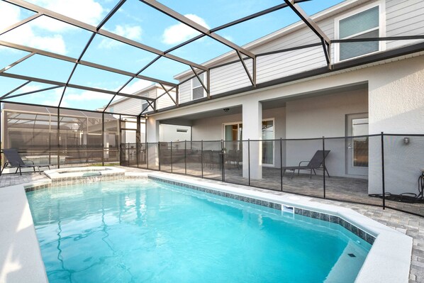 A swimming pool with a glass ceiling, surrounded by lounge chairs and a covered patio area.