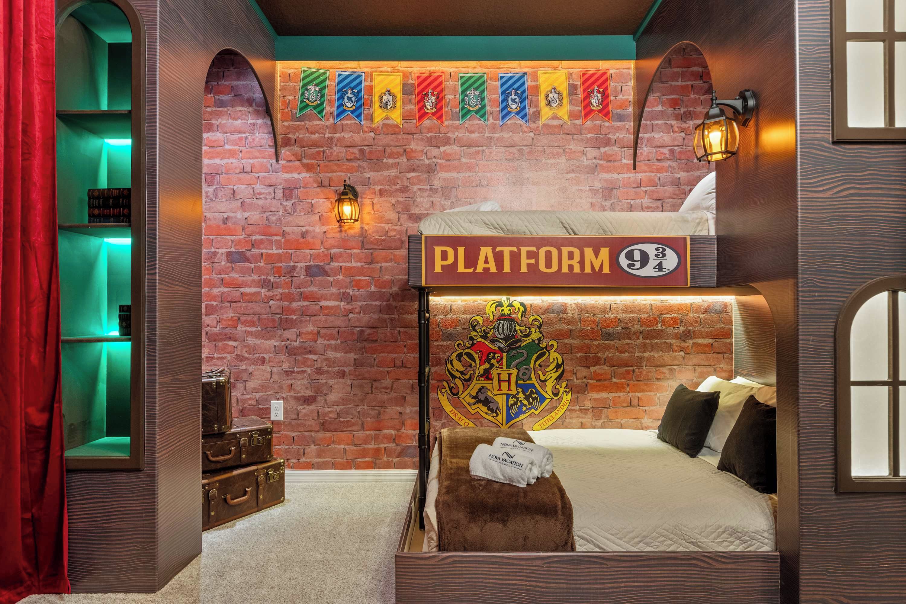 Ein thematisch gestaltetes Hotelzimmer mit Backsteinwand, einem Schild mit der Aufschrift „PLATFORM 9¾“ und einem Bett mit dem Hogwarts-Wappen.