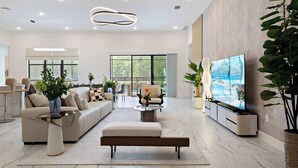 A spacious living room with a large TV, comfortable seating, and a view of the outdoors. - Grand 15-bedroom Villa -magical Themes, Pool & Game Loft, Lakeview (Kissimmee)