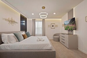 A modern bedroom with a large bed, a dresser, a television, and a decorative wall piece.