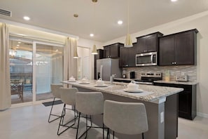 A modern kitchen with dark cabinets, a large island with bar stools, and a sliding glass door leading to a patio.