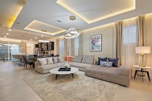 A modern living room with a sectional sofa, a coffee table, and a dining area with chairs and a table.
