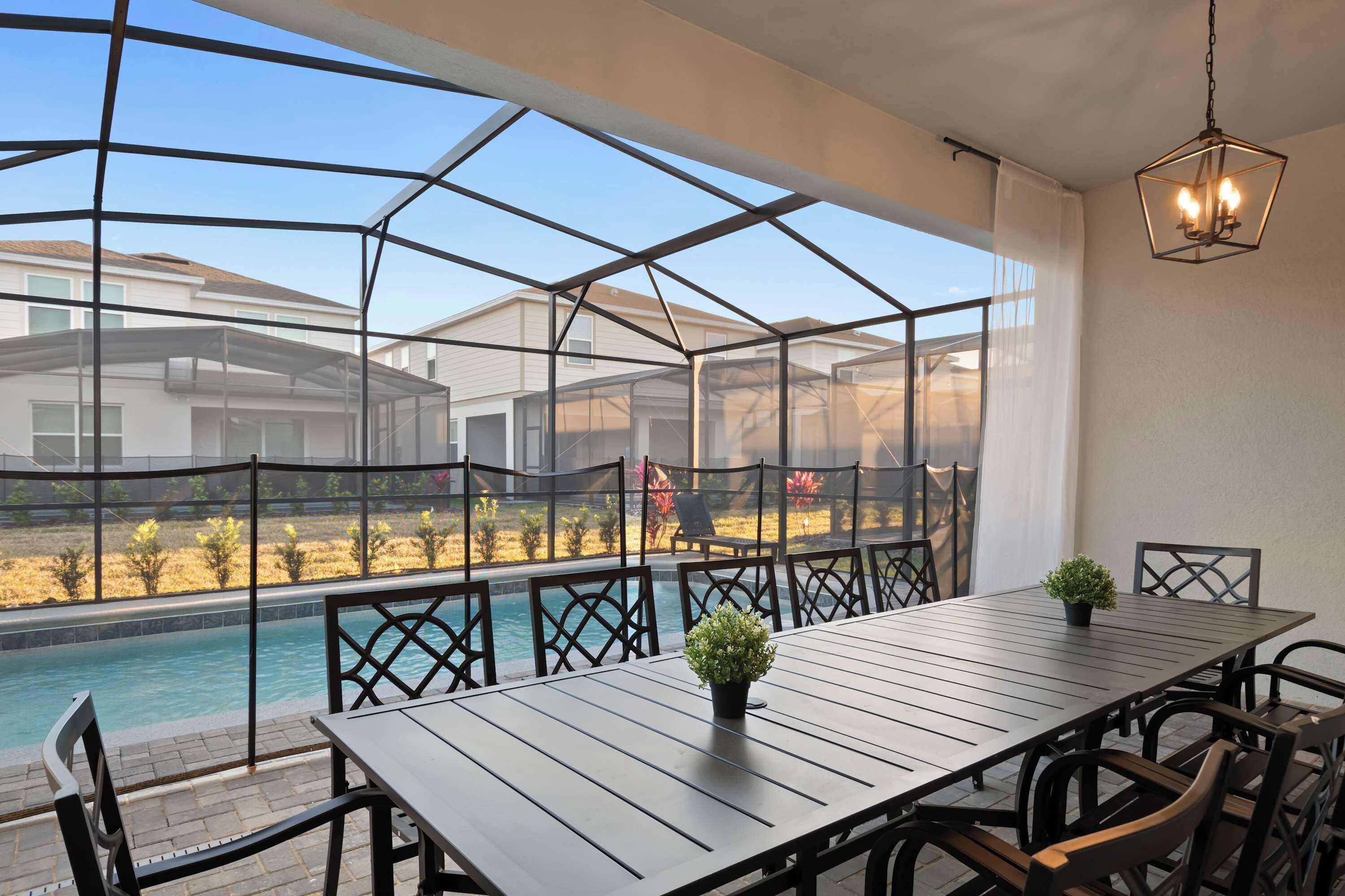 A covered outdoor dining area with a pool view, metal chairs, and a table with potted plants.