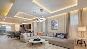 A modern living room with a sectional sofa, a coffee table, and a dining area with chairs and a table. - Luxurious Windsor Cay Villa Private Pool, Epic Game Room & Minutes to Disney! (Clermont)