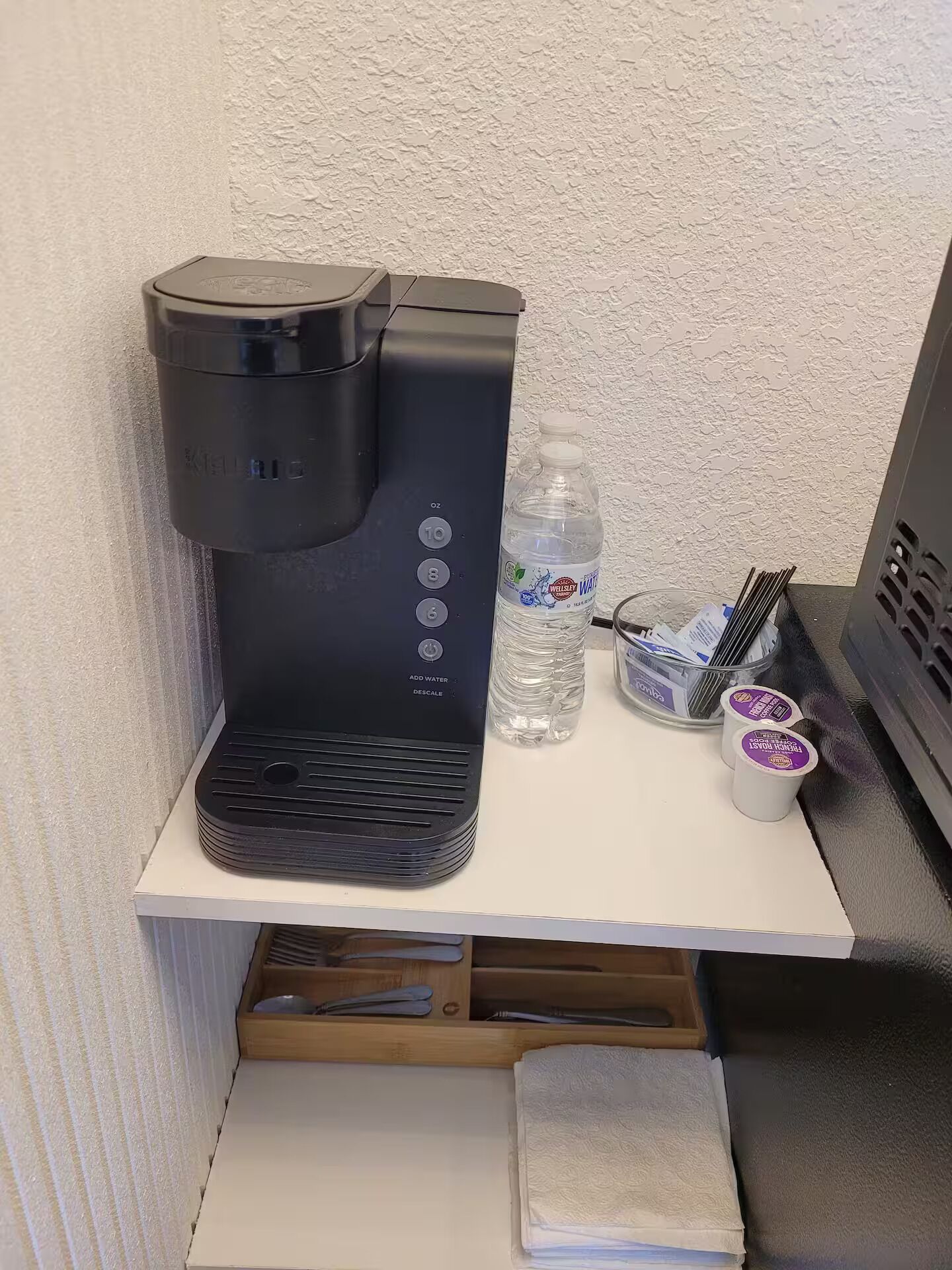 Een kleine keuken met een koffiezetapparaat, een waterfles en een bakje met bestek.