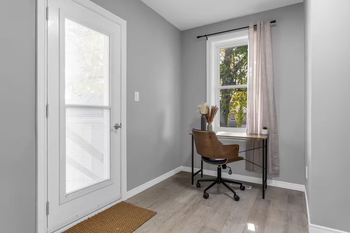 A room with a door, a window with blinds, a desk with a chair, and a curtain.