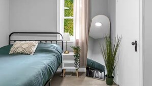 A bedroom with a bed, bedside table, lamp, mirror, and potted plant. - Spacious 3BDs - Close to Wineries, Brock & Falls! (Thorold)