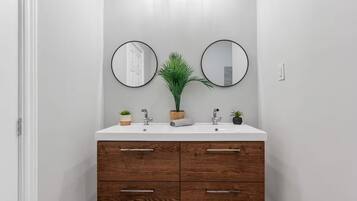 A bathroom with a white vanity, two round mirrors, a potted plant, and a wooden cabinet with drawers.