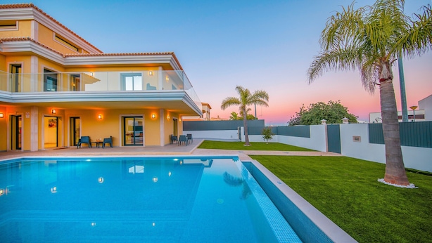 A modern two-story house with a swimming pool, outdoor seating, and a well-maintained lawn.