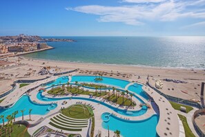 A resort with a large, winding pool surrounded by palm trees and sun loungers, overlooking a beach and the sea. - Luxury Studio at Sonoran Star Resort (Puerto Peñasco)