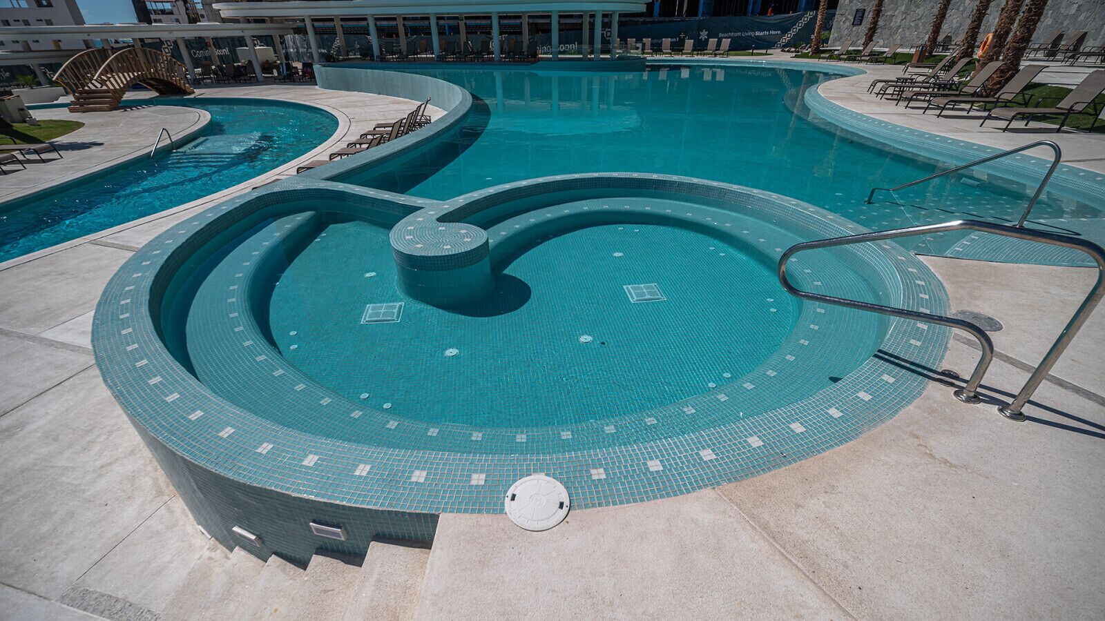A circular infinity pool with a central water feature, surrounded by lounge chairs and a stone deck.