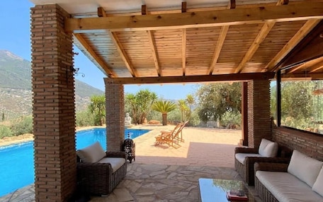A covered outdoor area with a pool, wicker furniture, and a view of the landscape.