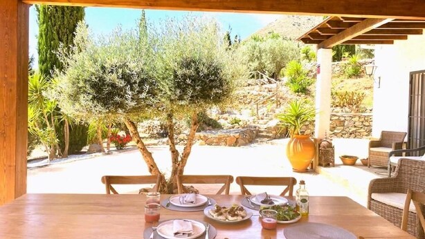 Un espace de restauration en plein air avec une table en bois prévue pour quatre personnes, entourée de chaises en osier.