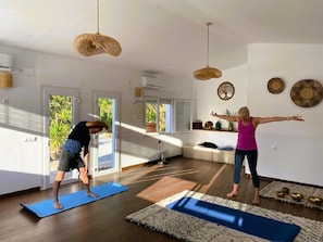 A room with large windows, a yoga mat, a woven light fixture, and decorative plates on the wall.