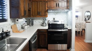 Cozinha moderna com armários de madeira, fogão de aço inoxidável e painel de proteção de mármore.