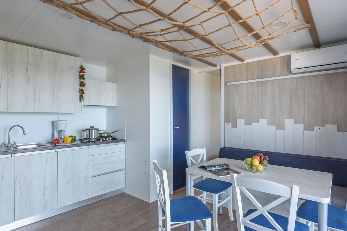 A modern kitchen with white cabinets, a built-in stove, and a dining area with a white table and blue chairs.