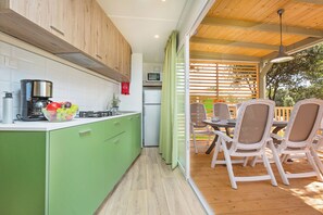 Een moderne keuken met groene kastjes, een koffieapparaat en een schaal met fruit. Er is een eethoek met witte stoelen en een tafel buiten, verbonden door een schuifdeur van glas.
