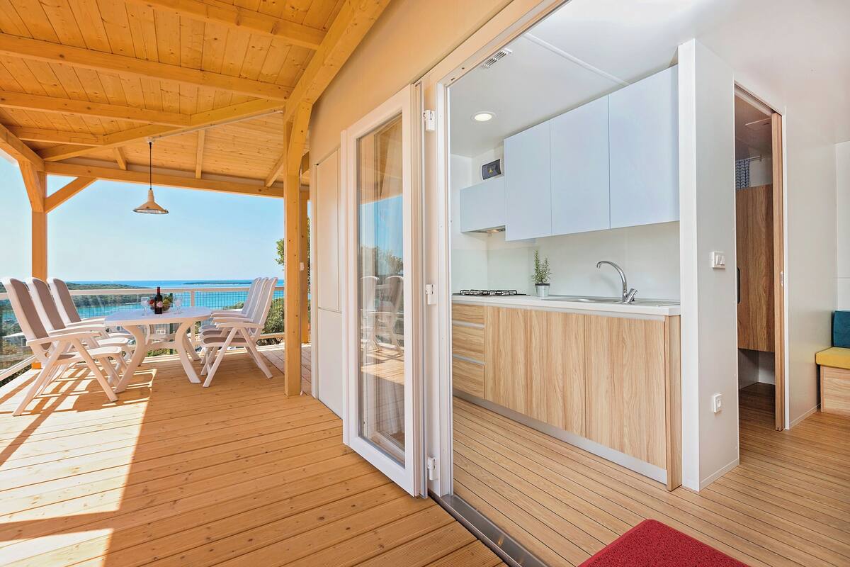 Een houten terras met een tafel en stoelen, een keuken met witte kasten, en uitzicht op zee.