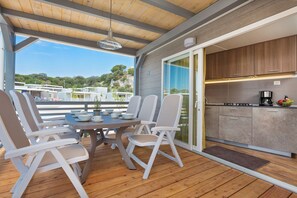 Un espacio comedor al aire libre techado con mesa y sillas, una cocina con armarios y electrodomésticos, y vistas del paisaje circundante.