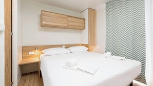 A modern hotel room with a wooden headboard, a bedside table with a lamp, a large bed with white linens, and a green patterned shower curtain. - Vestar Campsite Mobile Homes (Rovinj)