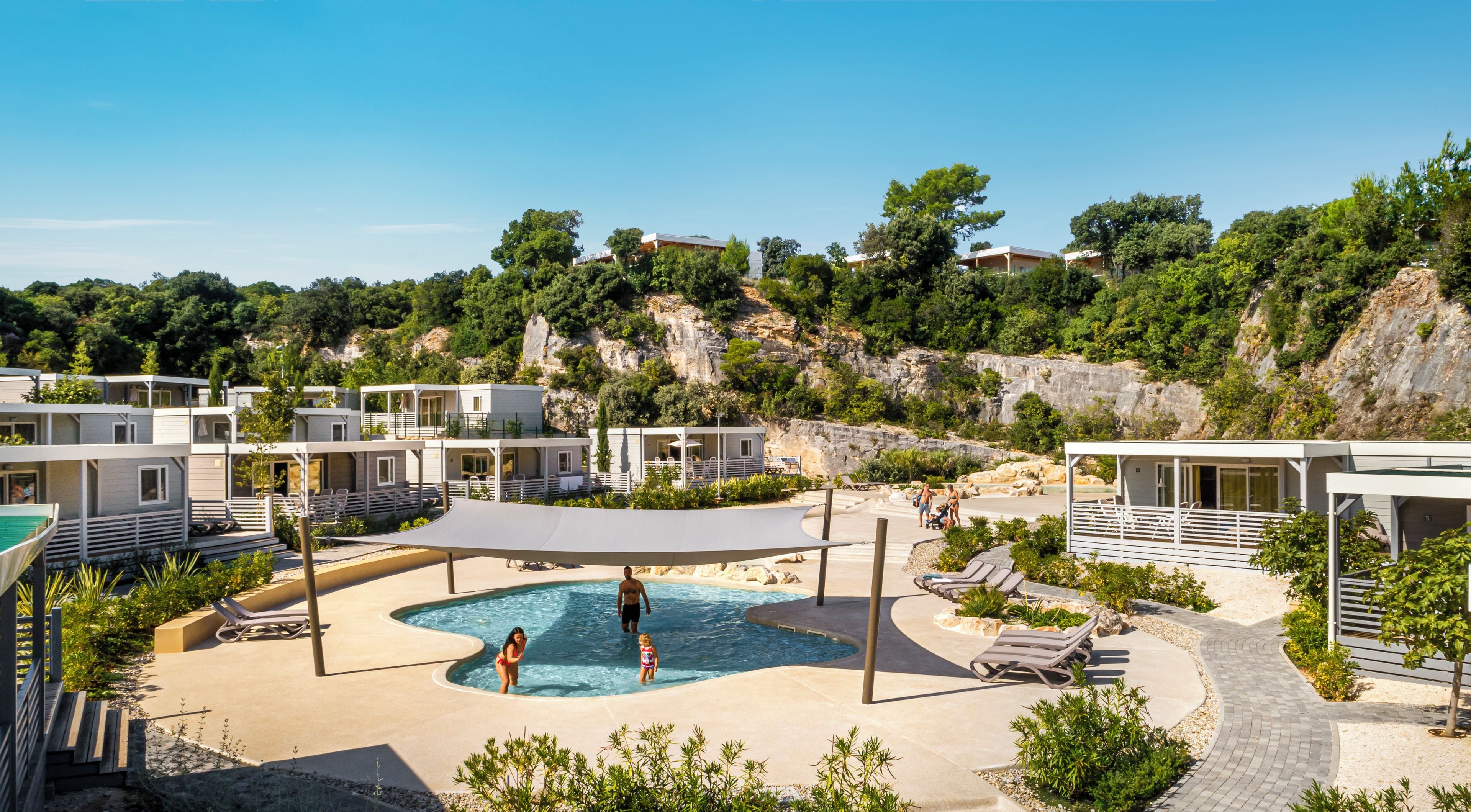 A resort with a swimming pool, sun loungers, and a view of the surrounding landscape.