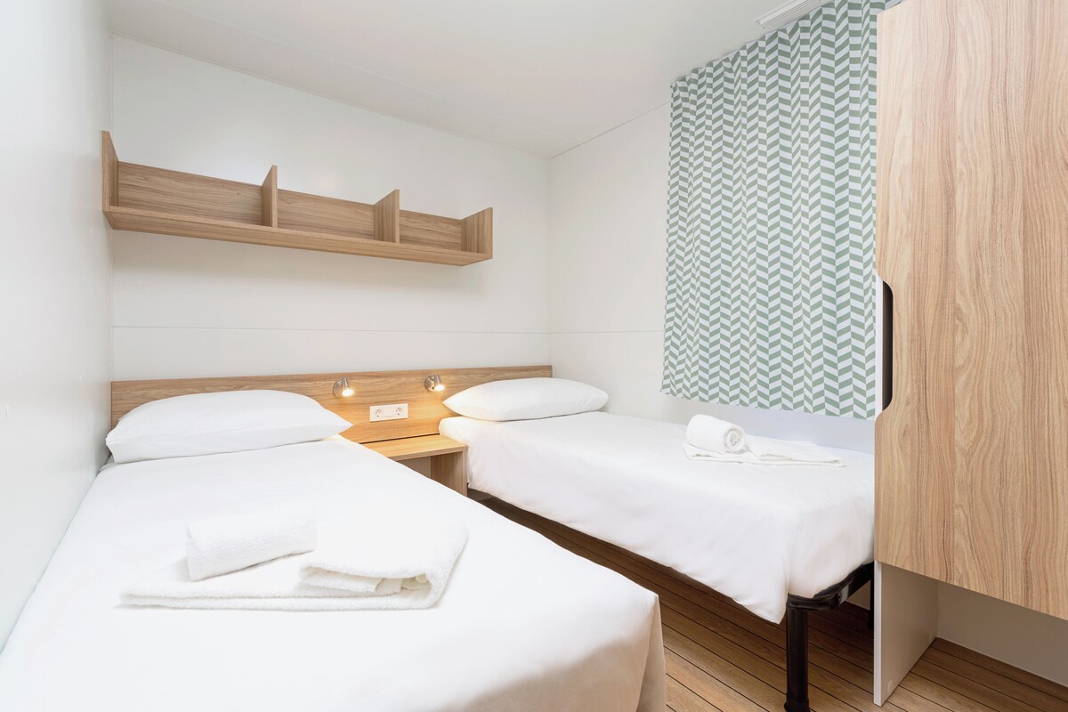 Een hotelkamer met twee bedden, houten hoofdeinden, een nachtkastje met een lamp en een kamerkleed met patroon.