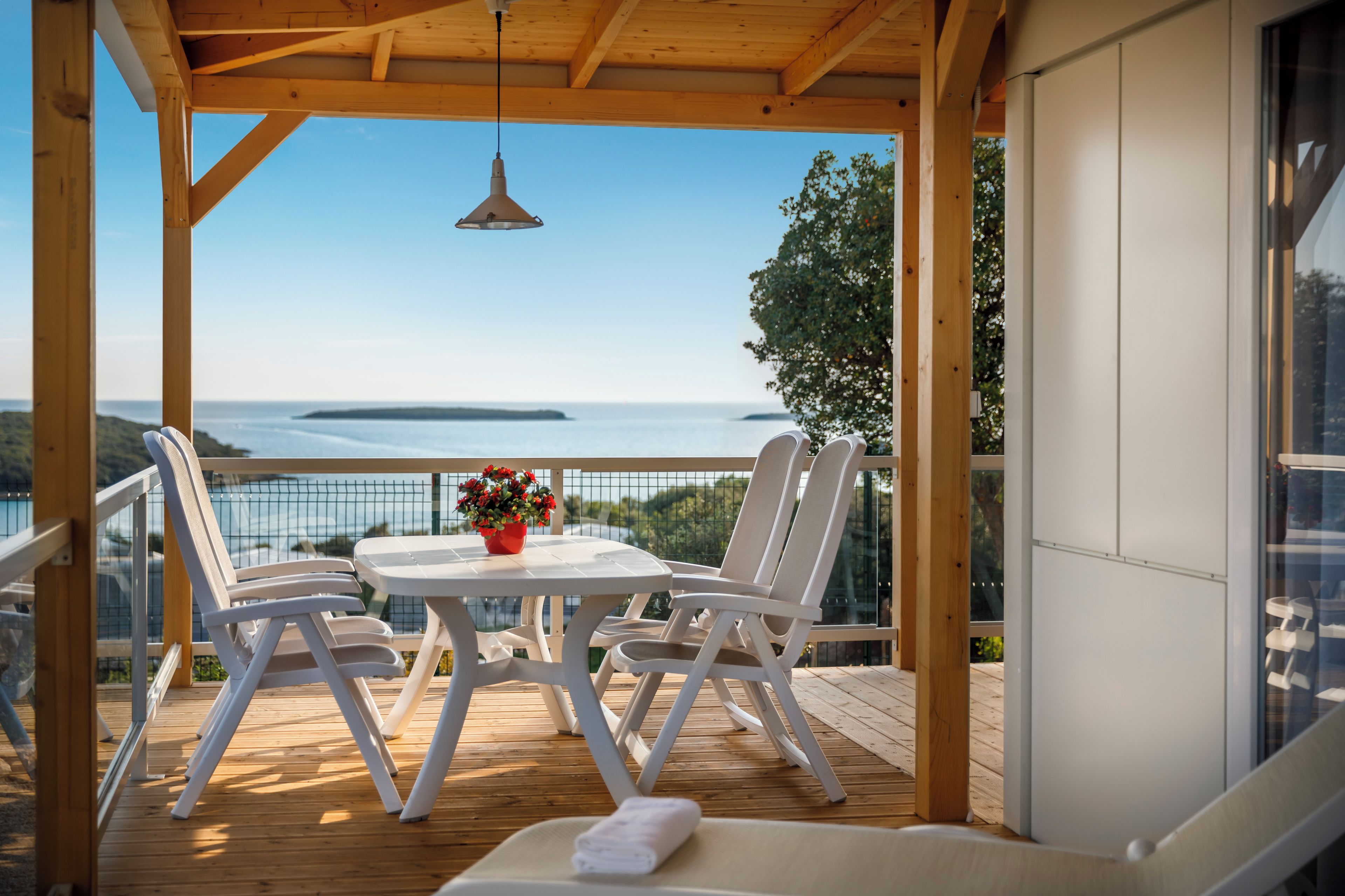 Eine Holzterrasse mit Tisch und Stühlen, mit Blick auf ein Gewässer und entferntes Land.