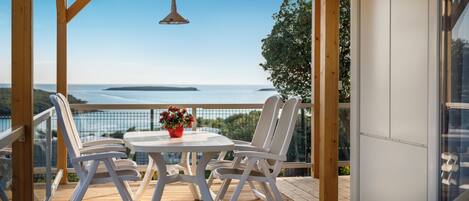 Eine Holzterrasse mit Tisch und Stühlen, mit Blick auf ein Gewässer und entferntes Land.